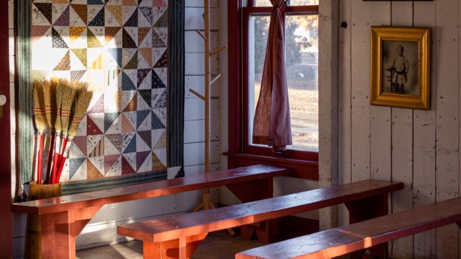 Habitación luminosa con bancos de madera, una colcha colgada en la pared, una foto antigua y cortinas en la ventana
