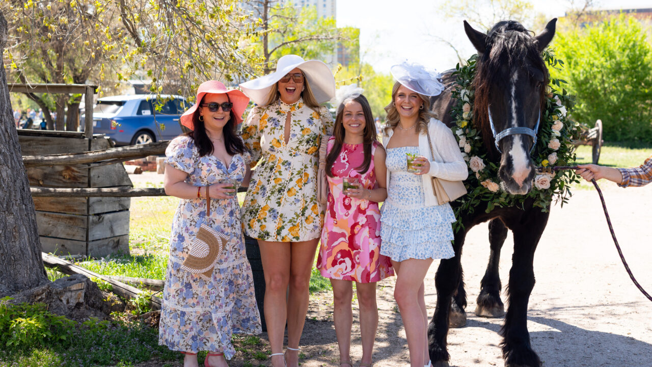 Mujeres con vestidos de flores y sombreros, sonriendo junto a un caballo engalanado