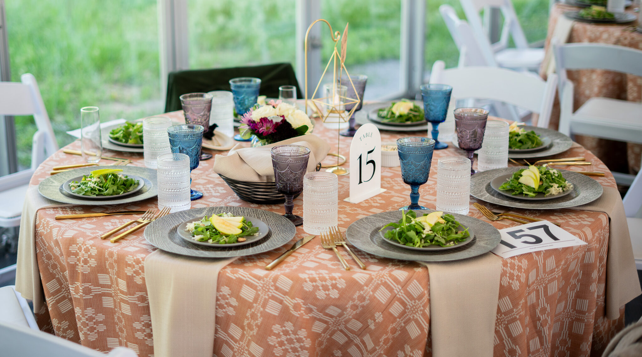 Elegant table setting with salad plates, blue and clear glasses, table number 15, and floral centerpiece