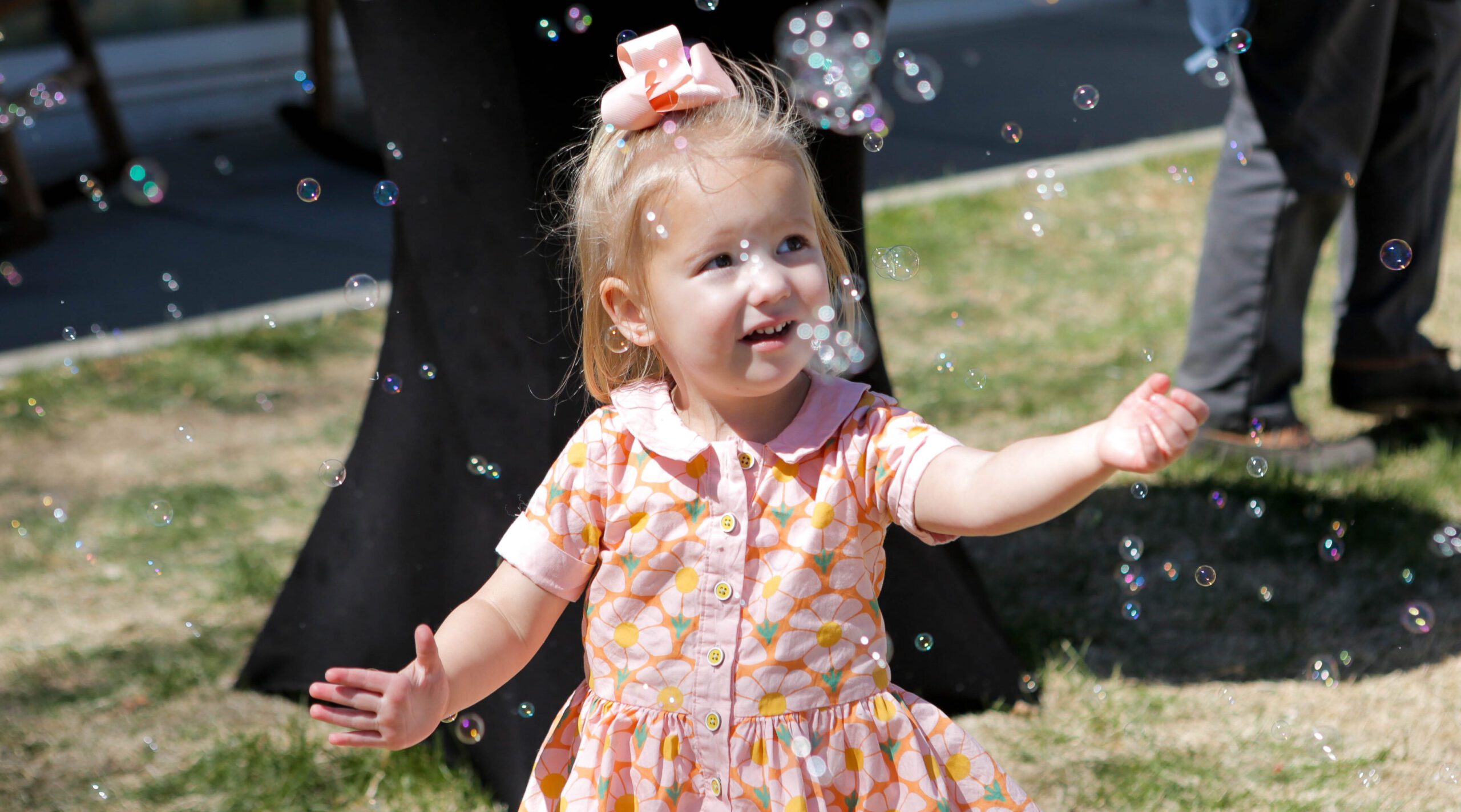 Una niña pequeña con un vestido rosa que juega alegremente con pompas de jabón al aire libre