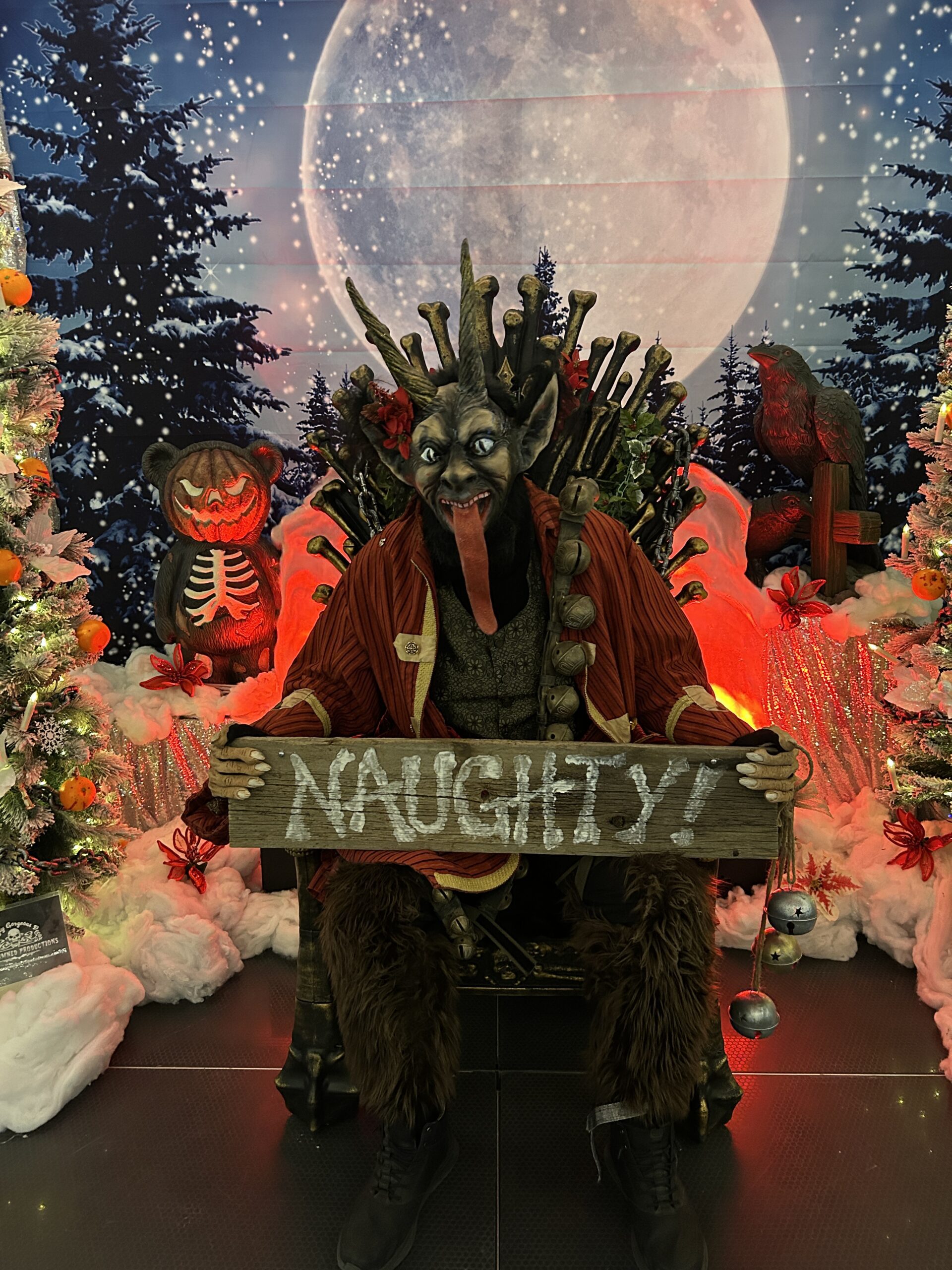 Character resembling Krampus holds "Naughty!" sign with festive snow and moon background