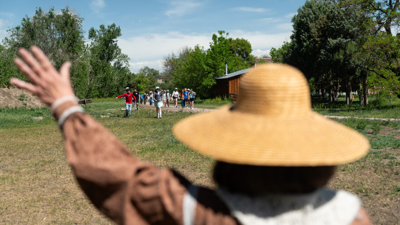 Person with straw hat waves at children walking on a trail