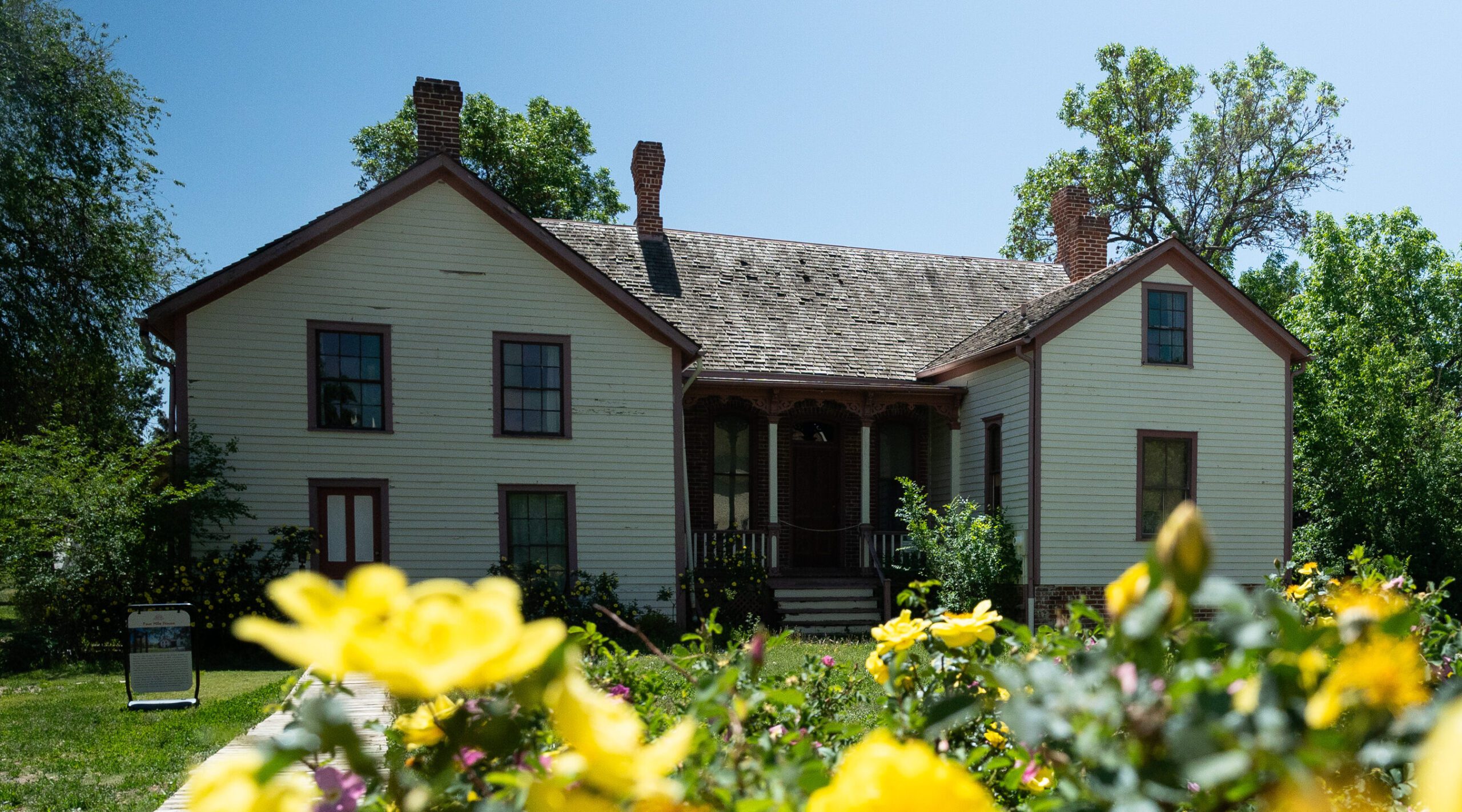 Historic wooden house with yellow flowers in foreground, surrounded by trees